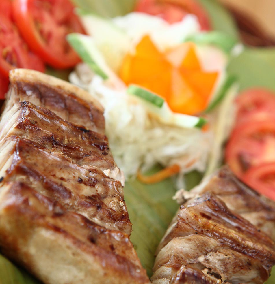Close-up of grilled meat skewers served with sliced tomatoes and shredded vegetable garnish on a banana leaf