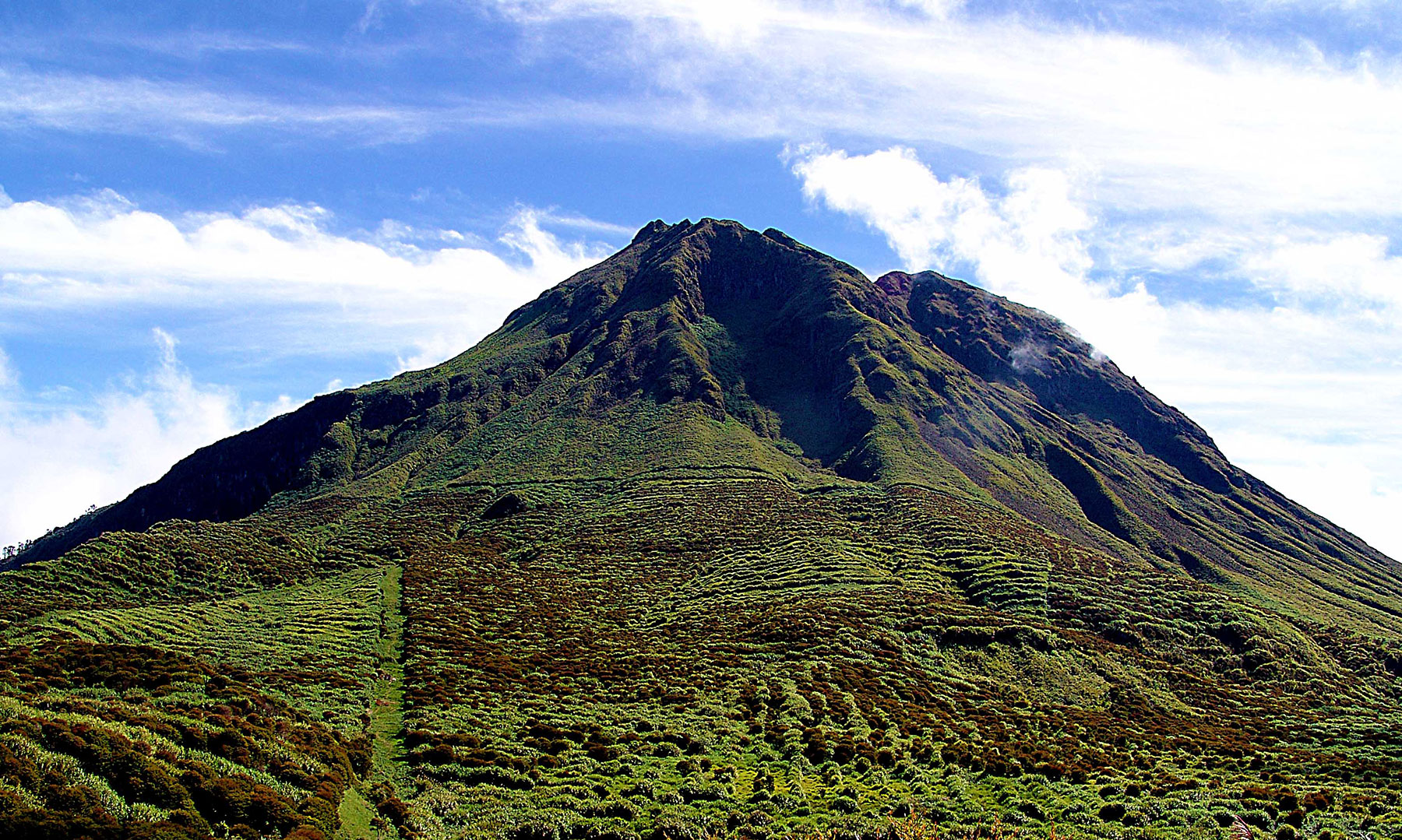 Large green mountain peak under blue sky with scattered clouds